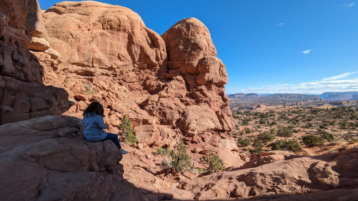 Une jeune fille est assise sous une arche devant le panorama d'Arches National Park