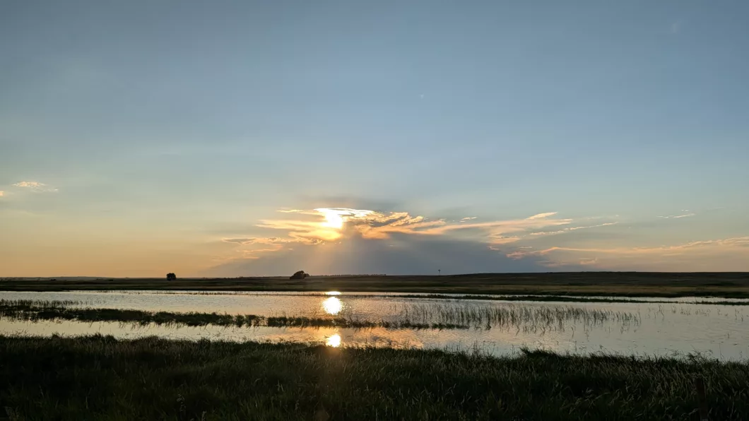 Le soleil commence à se coucher à l'horizon. Au premier plan, une rivière de la réserve de Lacreek